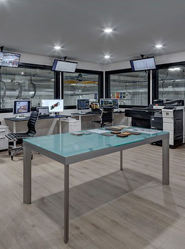 Offices Modern office with multiple desks, computers, and chairs. Large windows reveal an industrial setting outside. Central glass table on a wooden floor.