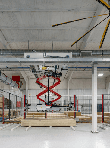 p4 Factory interior showing a red scissor lift, stacked wooden boards, industrial ductwork, a large yellow ceiling fan, and safety fencing.